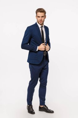 Zarafet, güven ve iş konsepti. Yakışıklı, sakallı, takım elbiseli ve kravatlı sarışın bir işadamı. Ceketini düzeltiyor. Kameraya bakıyor.