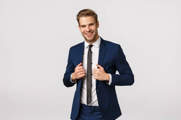 Fiducia, eleganza e business concept. Bello giovane uomo d'affari elegante in abito, regolazione giacca e sorridente, firmato molto e sensazione di successo arrivando le mani, sfondo bianco — Foto Stock