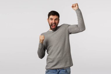 Yaşa! Heyecanlı ve mutlu bir adam, bir elini neşeyle kaldırır, şampiyon gibi yumruk atar, takımın galibiyetini kutlar gol atar, ödül kazanır, spor piyangosunda büyük bir teklif kazanır, beyaz arka planda zafer kazanır.