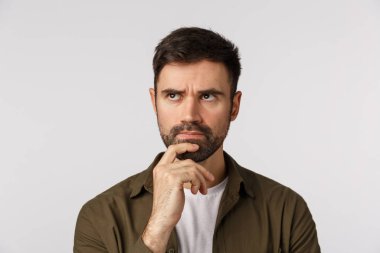 Yakın plan stüdyo dalgın sakallı genç adam, çene dokunuyor ve kaşlarını çatıyor düşünceli, düşünüyor, düşünüyor, karar veriyor, plan yapıyor, çözüm arıyor.