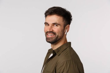 Yakından çekilen profil neşeli, arkadaş canlısı ve mutlu gülümseyen genç adam, gülmek ve gülümsemek için kameraya dön, müzik dinle kablosuz kulaklıklar, kulaklık, beyaz arka plan