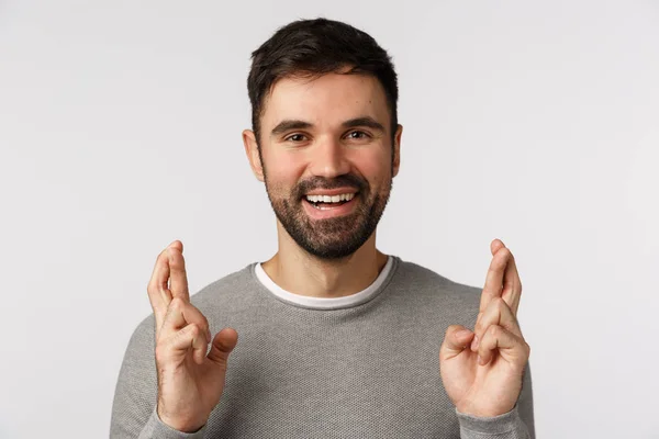 Close-up hopeful and cheerful, optimistic bearded adult guy in grey sweater, believe miracle happen, hope dream come true, cross fingers good luck, praying or relish deal went well, white background — Stock Photo, Image