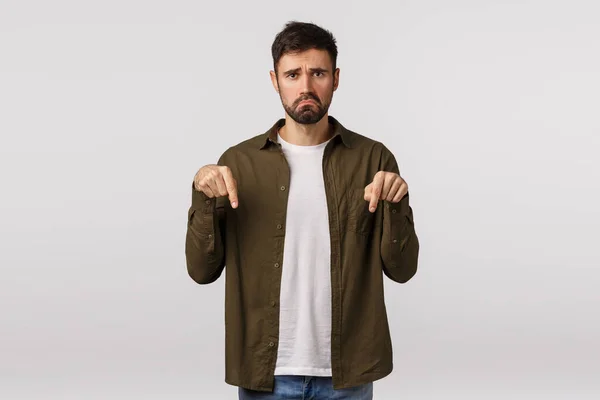 Man having disappointing bad news. Upset and miserable, unhappy young bearded man feeling regret or jealous, pulling sad grimace, frowning, pointing down complaining, white background — Stock Photo, Image