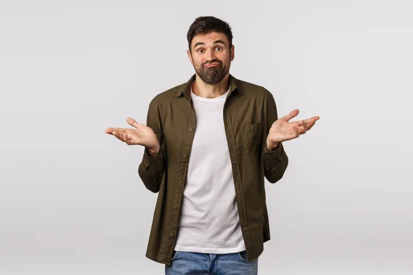 Sorry cant help. Indecisive and clueless handsome bearded man in coat, shrugging with hands sideways, smirk puzzled, dont know anything, trouble answer, standing white background troubled — Stock Photo, Image