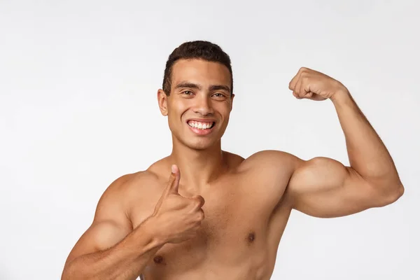 Adolescente afroamericano muestra músculos en el brazo. Aislado sobre fondo blanco. Retrato de estudio. Concepto de edad transitoria . — Foto de Stock