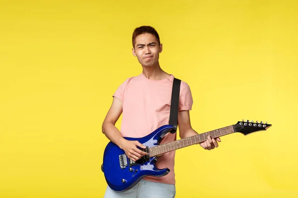 Handsome young musician playing the guitar and singing, isolated on yellow background