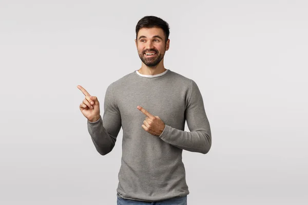 Agradado encantador sorte jovem bonito macho, adulto em camisola cinza, apontando para a esquerda, observar cena bonito, variante escolhido, ver boa escolha, feliz e encantado, sorrindo satisfeito — Fotografia de Stock