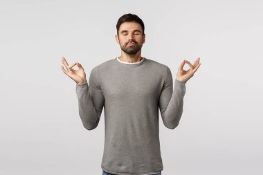 Sabır, rahatlama ve meditasyon konsepti. Barışçıl, genç, yakışıklı, sakallı, zihnini ve vücudunu genişleten, hislerini besleyen, el kaldıran, yoga yapan, kapalı gözlerle nefes alma alıştırması yapan adam.