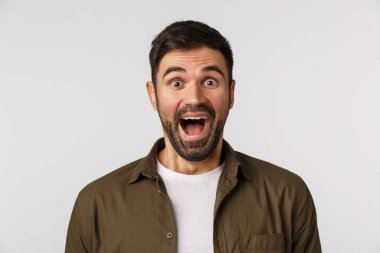 Neşeli, genç, kaygısız, beyaz sakallı erkek arkadaş çocuk gibi seviniyor ya da tezahürat yapıyor, mutlu gülümsüyor, eğlenceli bir şey görüyor, lunaparkta eğleniyor, neşeli bir şekilde ayakta duruyor.