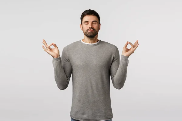 Patience, relaxation and meditation concept. Peaceful young handsome bearded guy broaden mind and body, feeling zen, raise hands mudra gesture, practice breathing yoga with closed eyes — Stock Photo, Image