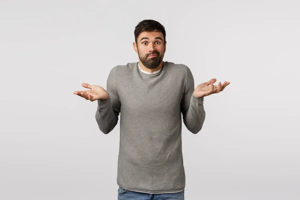 Guy asking help dont know what do. Perplexed, confused and indecisive cute clumsy bearded man in grey sweater, raise hands sideways, shrugging clueless, cant help, cannot answer, smirk saying sorry — Stock Photo, Image