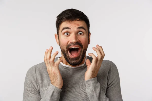 Excité, joyeux et optimiste bel homme barbu en pull gris, entendre des nouvelles étonnantes, serrer la main près du visage et crier étonné, gagner, recevoir le prix, atteindre l'objectif, fond blanc — Photo