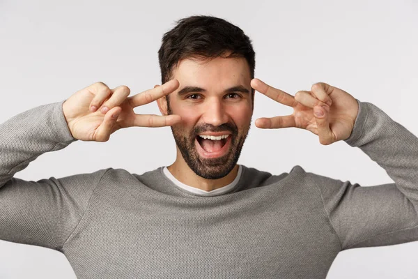 Despreocupado, atrevido e animado gay feliz homem com barba, usar camisola cinza, mostrar gesto disco, sinais de paz sobre os olhos e sorrindo, gritando otimista, se divertindo, orando nas férias, fez bom negócio — Fotografia de Stock