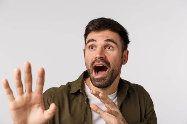 Scared and anxious bearded guy screaming as something falling on him, raising hands to defend himself, staring upper left corner bending in danger situation, standing frightened white background — Stock Photo, Image
