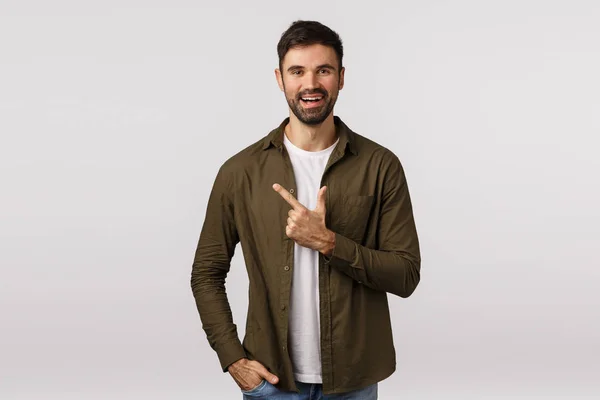 Alegre, cara bonito barbudo amigável em roupa moderna, apontando para a esquerda, apresentar pessoa aos amigos ou recomendar loja lugar, escolher o produto, sorrindo alegremente, fazer reserva, fundo branco — Fotografia de Stock