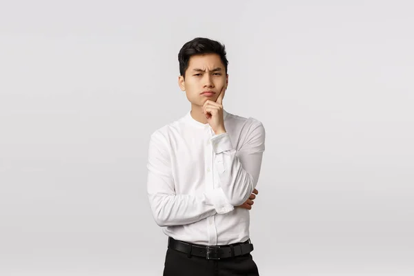 Suspicious and skeptical, thoughtful attractive asian man in shirt, pants, frowning look camera with disbelief and serious face, touch chin, thinking, have assumptions, standing white background — Stock Photo, Image