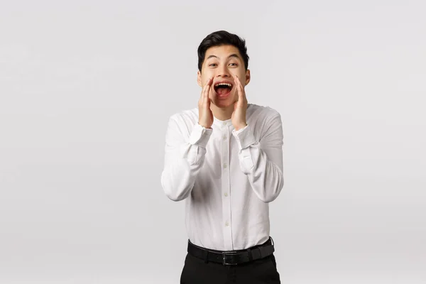 Oye, ven aquí. Alegre sonriente feliz asiático chico buscando nuevos empleados a la empresa, contratar, tomarse de la mano cerca de la boca abierta gritando nombre, buscando a alguien, de pie fondo blanco — Foto de Stock