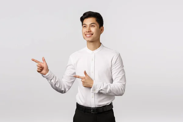 Alegre y determinado joven asiático hombre de negocios hecho en su mente, listo tomar una decisión, señalando mirando a la izquierda y sonriendo con aprobación, como lo que ve, la elección de gran producto, fondo blanco — Foto de Stock