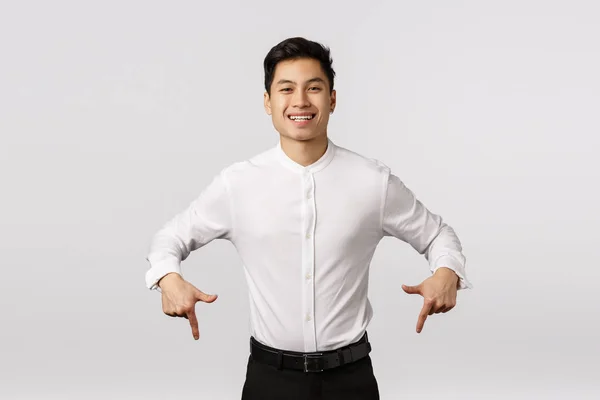 Despreocupado, sonriente lindo y alegre asiático millennial chico en formal desgaste, camisa y pantalones, apuntando hacia abajo, invitando a la salida, visita página del evento, sitio de compras o pancarta corporativa, sonriendo regocijo — Foto de Stock