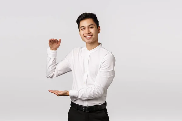 Radostný dobře vypadající asijský muž podnikatel, zaměstnanec v bílé košili, kalhoty, ukazuje velký box s potěšeným výrazem, držení produktu nebo něco velkého a uspokojující, stojí bílé pozadí — Stock fotografie