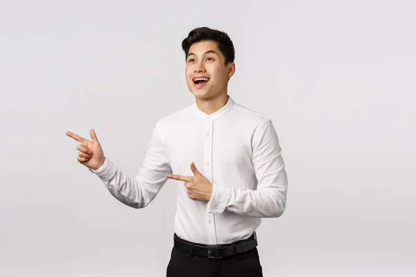 Indrukwekkend dromerig en benieuwd schattig aziatische man in business outfit, wijzend naar links, overwegen iets prachtig of mooi, blij met een goede keuze, eindelijk gevonden perfect cadeau — Stockfoto