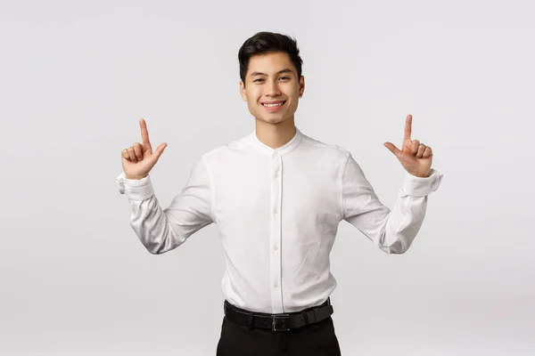 Hansdome asiático hombre de negocios en camisa blanca, pantalones negros, señalando con los dedos hacia arriba y sonriendo con la expresión complacido, satisfecho o contento, mostrando el producto, promoviendo banner corporativo, fondo blanco — Foto de Stock