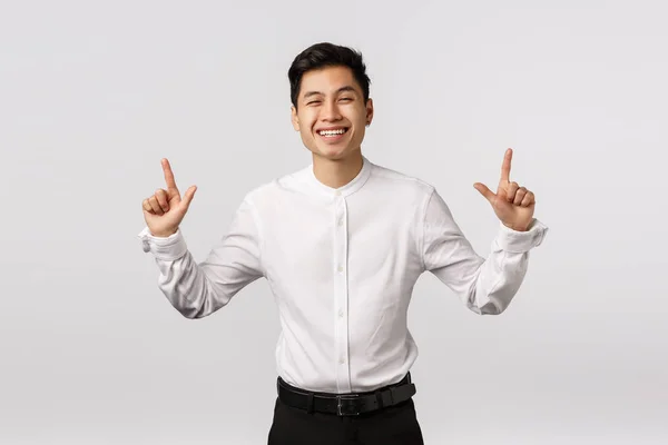 Concepto de felicidad, bienestar y éxito. Alegre lindo asiático chico en camisa blanca, pantalones negros, sonriendo y riendo felizmente, compartiendo emociones positivas y señalando hacia arriba en el banner del producto — Foto de Stock