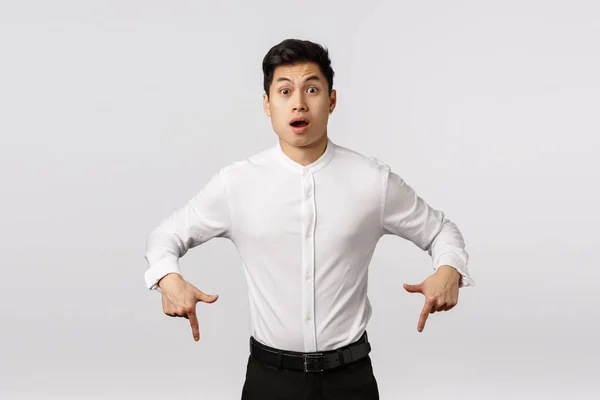 Freak out, alarmed and surprised shocked asian handsome guy in collar shirt, pants, pointing down, gasping amazed and speechless, say wow, hear strange unexpected news, white background — Stock Photo, Image
