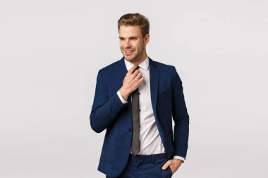 Şık, kendine güvenen, iddialı, klasik takım elbiseli yakışıklı erkek girişimci şirket yemeği, iş toplantısı, kravatını düzeltme ve şanslı, kararlı bir gülümsemeyle başka tarafa bakma.