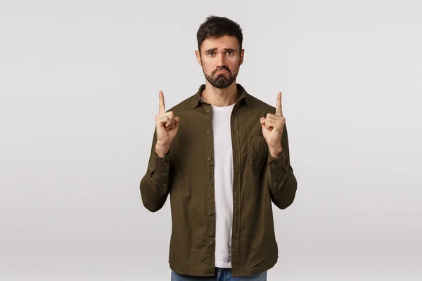 Sad and distressed lonely, miserable handsome bearded male in coat, pulling grimace with jealous, regret face, frowning pointing fingers up, telling disappointing bad news, complain, white background — Stock Photo, Image