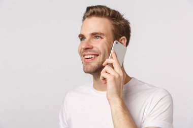 Rüya gibi ve kaygısız yakışıklı, gülümseyen, mavi gözlü çekici sarışın, yurtdışından evi arayan, mutlu, mutlu, mutlu, sırıtan kız arkadaş sesi, uzaklara bakan, akıllı telefonu kulağının dibinde tutan.