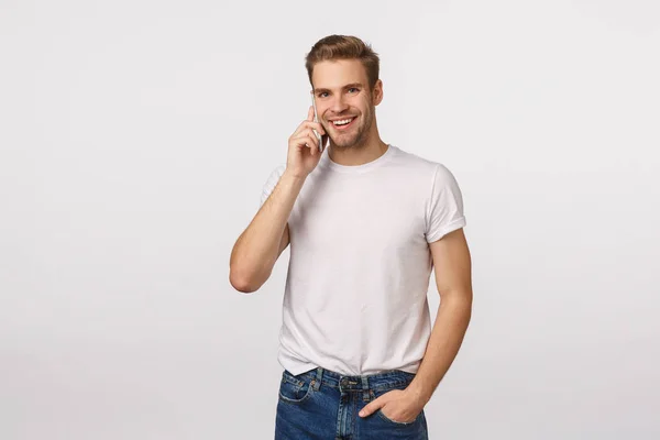 Zakelijk, technologie en modern lifestyle concept. Knappe zorgeloze lachende macho man met blond haar, borstel, nonchalant telefoneren, smartphone dicht bij het oor houden, grijnzende camera, witte achtergrond — Stockfoto