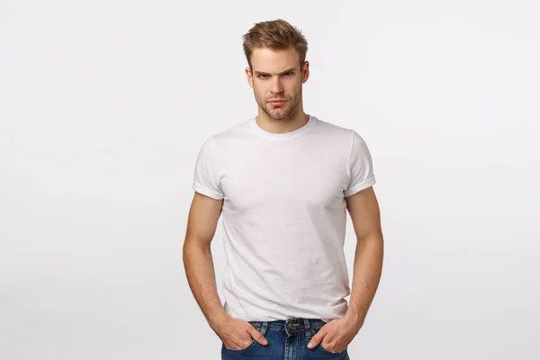 Angry, judgemental handsome macho blond male model in white t-shirt, look offended or angry, squinting aggressive, judging or being disappointed, standing suspicious, have doubts, white background — Stock Photo, Image