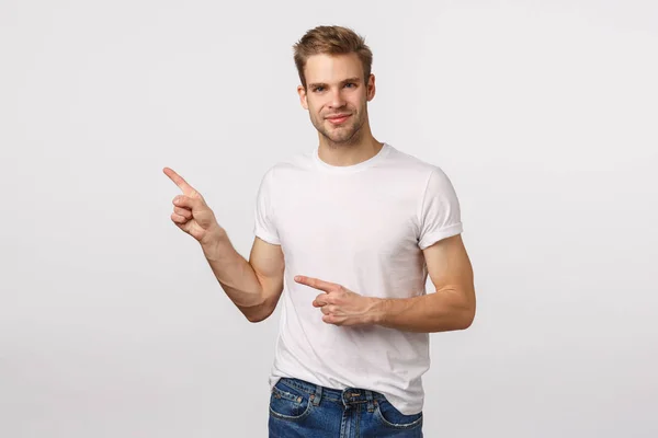 Knap, assertief tevreden jonge blonde man met haar, wijzen linksboven, glimlachen als uitziende partner, bespreken zakelijke concepten, suggereren product, raden plaats, witte achtergrond — Stockfoto