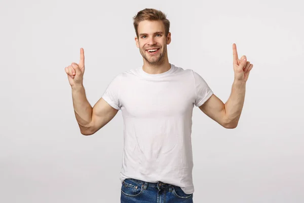 Dromerig blij goed uitziende blonde man met baard in wit t-shirt, wijzende vingers omhoog en lachend onder de indruk, wordt opgetild, hebben inspiratie uit het bijwonen van geweldig evenement, raden — Stockfoto