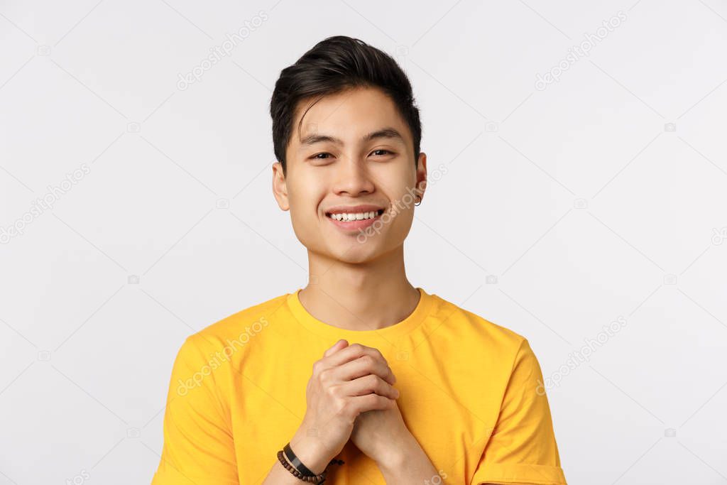 Close-up shot grateful, cute chinese hipster guy in yellow t-shirt, clench hands together over chest in thankful or touched pose, smiling delighted, gladly receive praises, white background