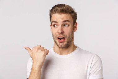 Meraklı, yakışıklı, beyaz tişörtlü, sarışın ve sakallı bir adam. Şaşırmış ve sola bakıyor. İlginç ürünler görüyor, tanıtım yapıyor, soru soruyor.