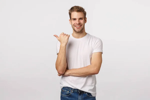 Dit moet je zien. Zorgeloos, casual knappe blonde blanke man met baard, duim naar links gericht en glimlachend tijdens gesprek over gezelschap, product of banner, aangeven waar te vinden — Stockfoto