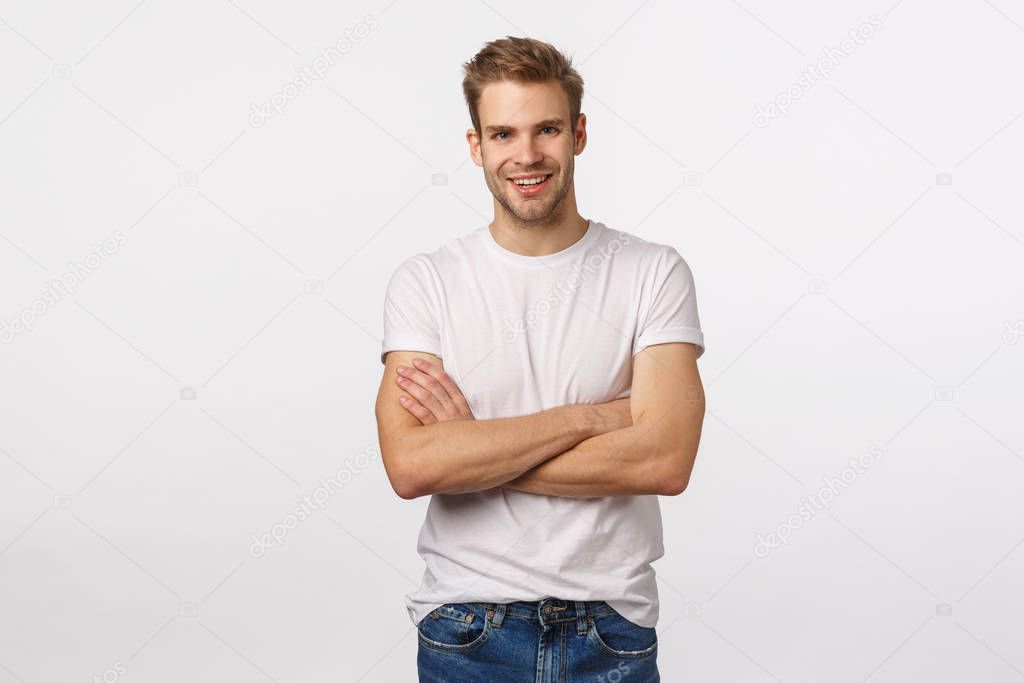 Enthusiastic, happy smiling blond man with bristle, white t-shirt, jeans, cross arms chest and grinning amused, hear interesting story, accepting good idea, agree with person, white background