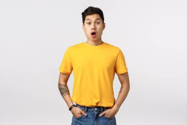 Şaşırmış, nutku tutulmuş, çok etkilenmiş sarı tişörtlü, soluk soluğa kalmış, ağzı açık, hayrete düşmüş, inanılmaz reklam afişine bakmadan hayrete düşmüş, beyaz arka planlı Asyalı yakışıklı çocuk.