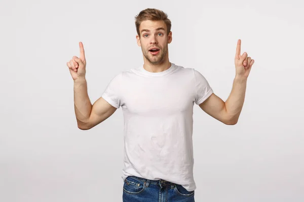 Je moet het zeker downloaden. Amuased aantrekkelijke en opgewonden, verbluft blond schattig baard man in wit t-shirt, wijzende vingers omhoog, hijgend verbaasd, sprakeloos, zie iets interessants — Stockfoto