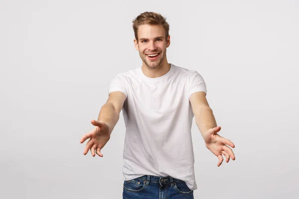 El hombre sugiere echar una mano, ayudar a llevar algo. Chico rubio carismático alegre con cerdas, extender las manos para coger o sostener algo, sonriendo feliz, de pie fondo blanco amistoso —  Fotos de Stock