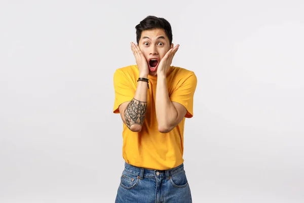 Impressed, shocked young asian man hear outstanding news, holding hands on cheeks, drop jaw scream from amazement and excited, see something stunning and cool, standing white background — Stock Photo, Image