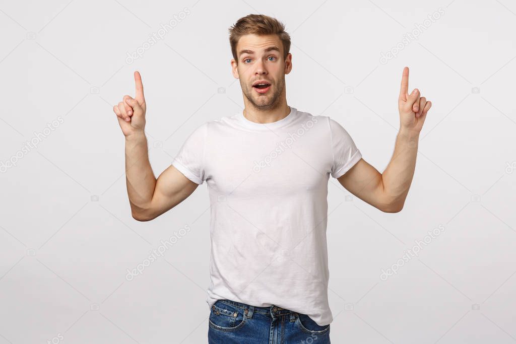 You certainly need download it. Amuased attractive and excited, astounded blond cute bearded man in white t-shirt, pointing fingers up, gasping astonished, speechless, see something interesting