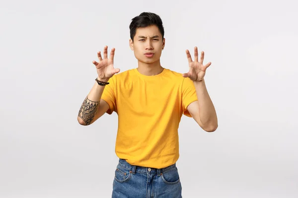 Řvoucí horký personál. Drzý a pohledný stylový asijský muž ve žlutém tričku, dělá gesto tlapky, jako by něco mačkal nebo předstíral tygra, šilhal drze a stál na bílém pozadí — Stock fotografie