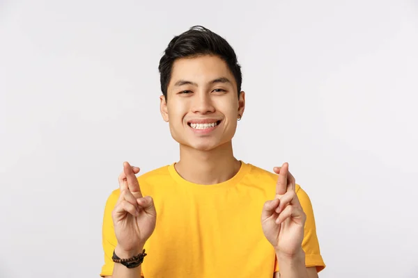 Vertrauen in dich. fröhlich und optimistisch junger asiatischer Mann in gelbem T-Shirt, betet für die Erfüllung eines Traums, genießt Erfolg oder gutes Geschäft, lächelt hoffnungsvoll, drückt die Daumen viel Glück, antizipiert — Stockfoto