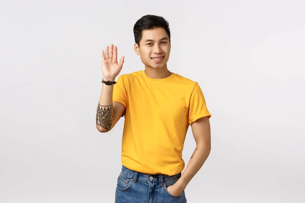Dost canlısı Asyalı erkek öğrenci yurtta yeni bir oda arkadaşı ediniyor, elini kaldırıyor merhaba, jest, selamlama arkadaşı, beyaz arka planda duran, tesadüfen biriyle buluşuyor. — Stok fotoğraf