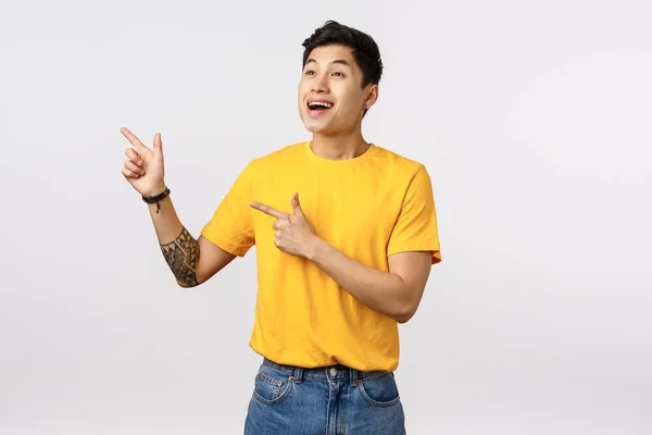 Neşeli, mutlu ve eğlendirici sarı tişörtlü yakışıklı Asyalı genç adam, güzel bir performans sergiliyor, şaşkınlık ve mutlulukla bakıyor, sol üst köşeyi işaret ediyor, beyaz arka plan — Stok fotoğraf