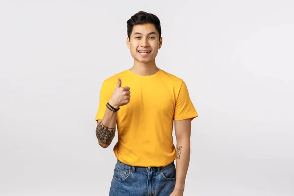 좋은 생각입니다. 해 보죠. 열정적으로 잘 생긴 아시아 문신을 한 남자가 노란 티셔츠를 입고 손을 들고 승인하는 모습을 보여 줍니다. 몸짓처럼 고개를 끄덕이며 동의하고 하얀 배경에 동의합니다. — 스톡 사진