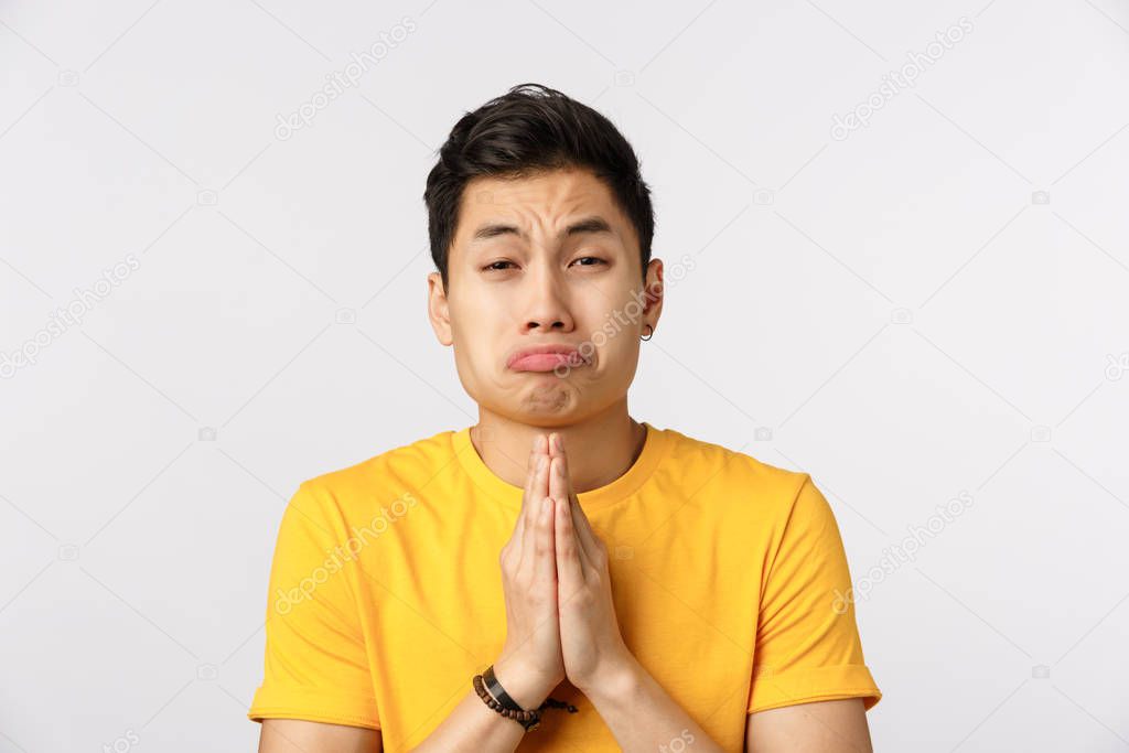 Clingy friend begging for favour with silly puppy look and pouting expression. Asian young man press hands together in pray, squinting asking mercy, say please, asking help, white background